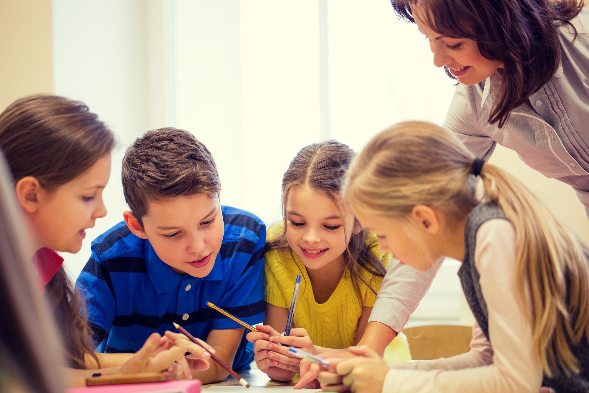 A group of children are sitting around a table with their teacher.