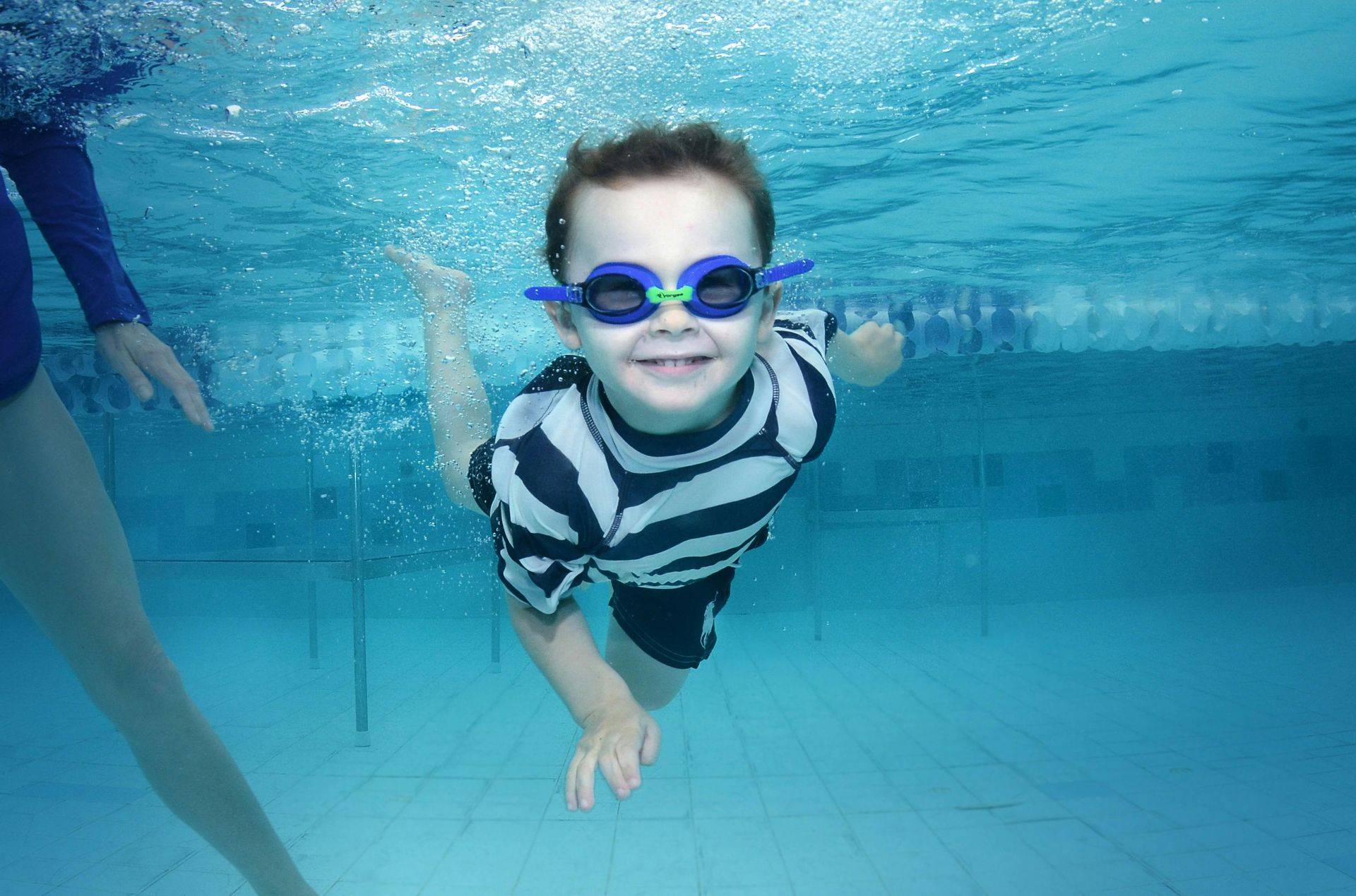 A young boy wearing goggles is swimming underwater in a pool.