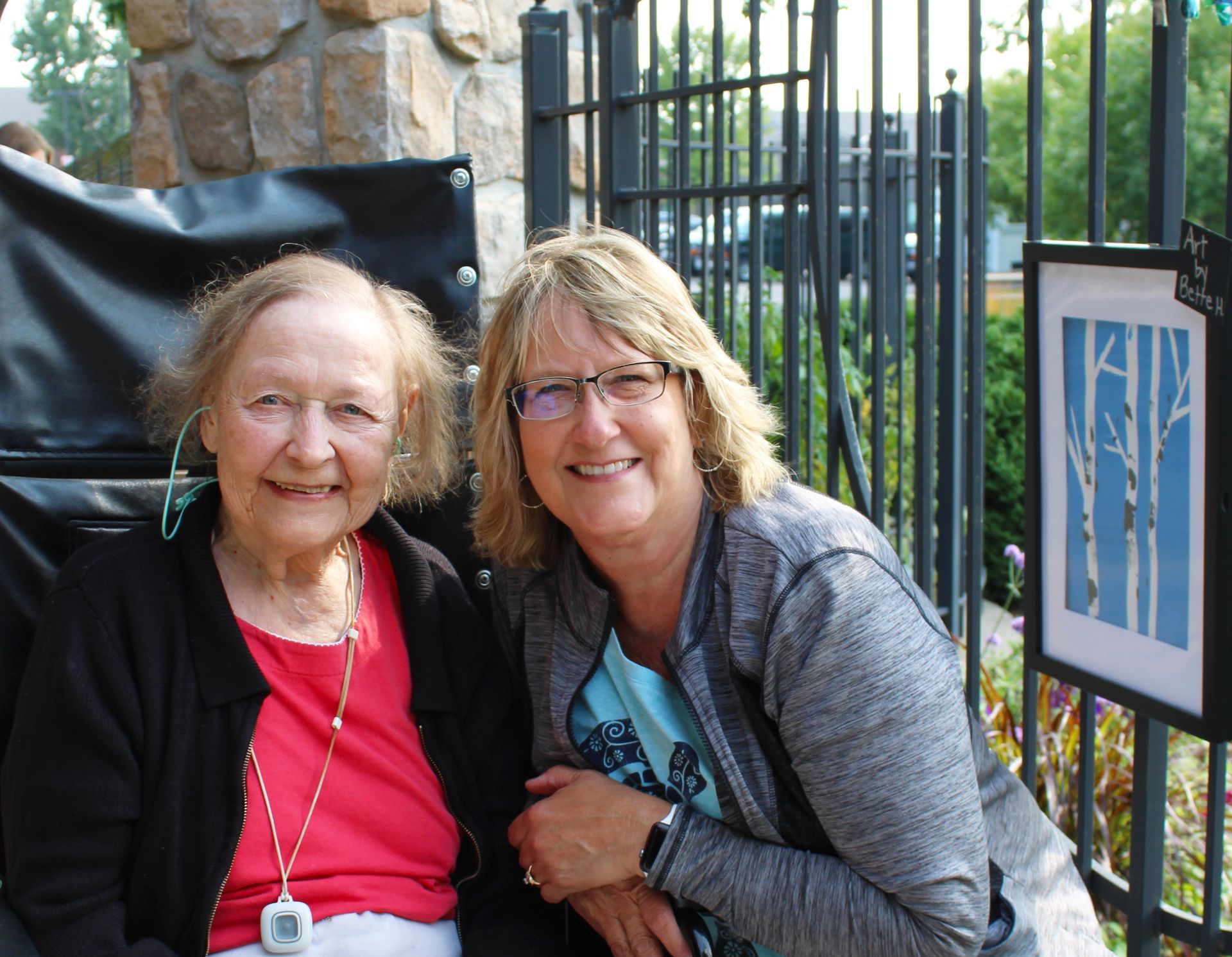 Two women are posing for a picture in front of a fence