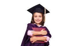 A little girl in a graduation cap and gown is holding a book.