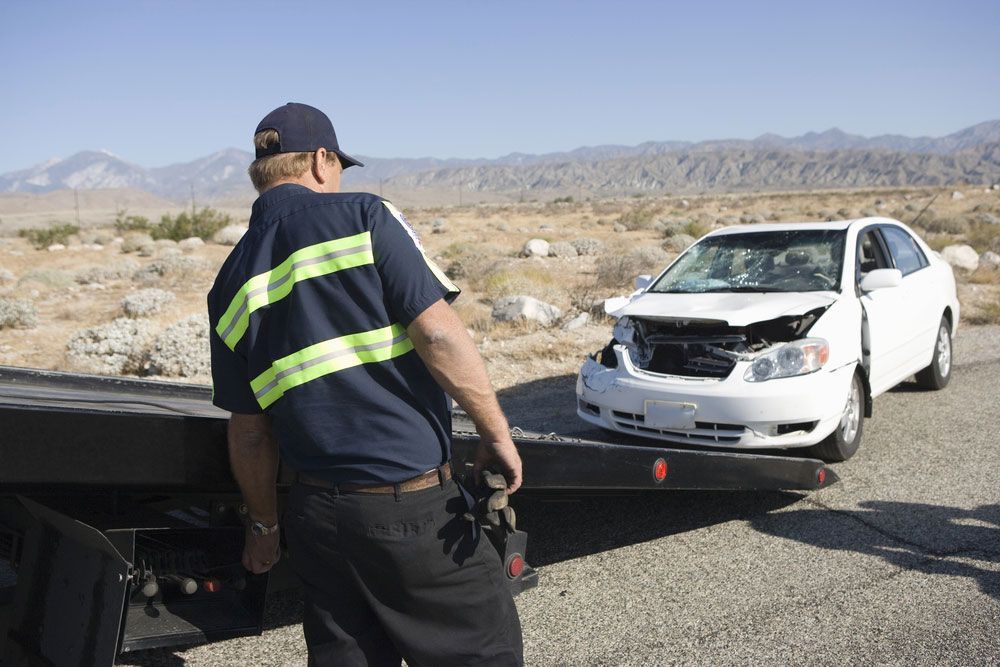 A Man Is Standing Next To A Tow Truck With A Broken Car On It — Tim's Towing and Transport In Gresford, NSW