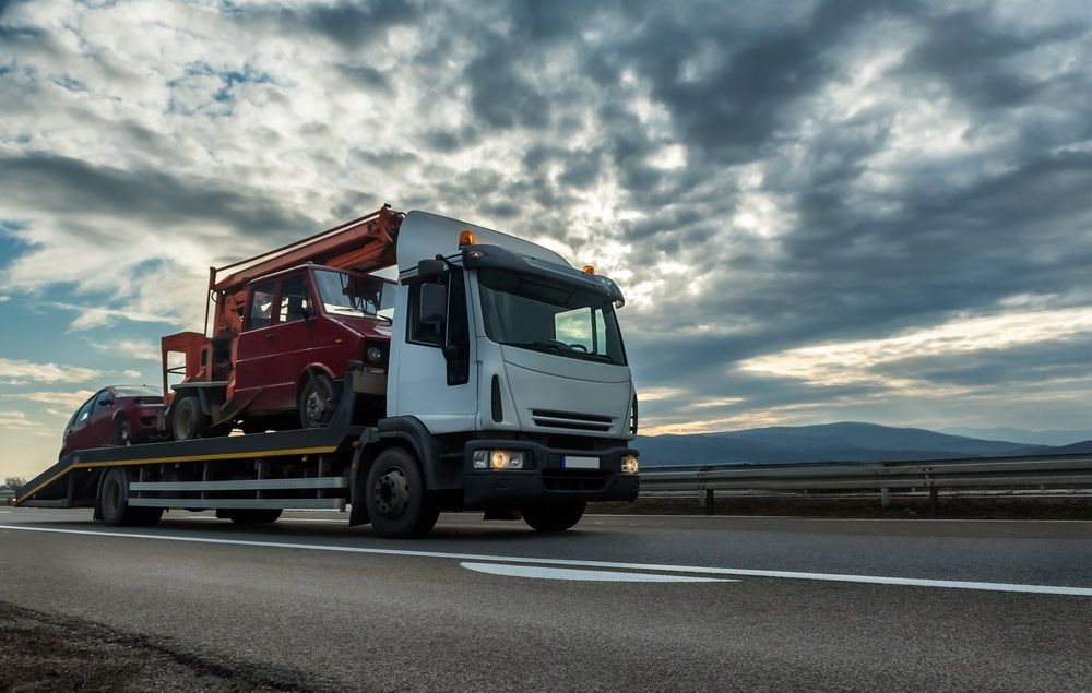 A Tow Truck Is Carrying A Red Car On A Highway — Tim's Towing and Transport In Hexham, NSW