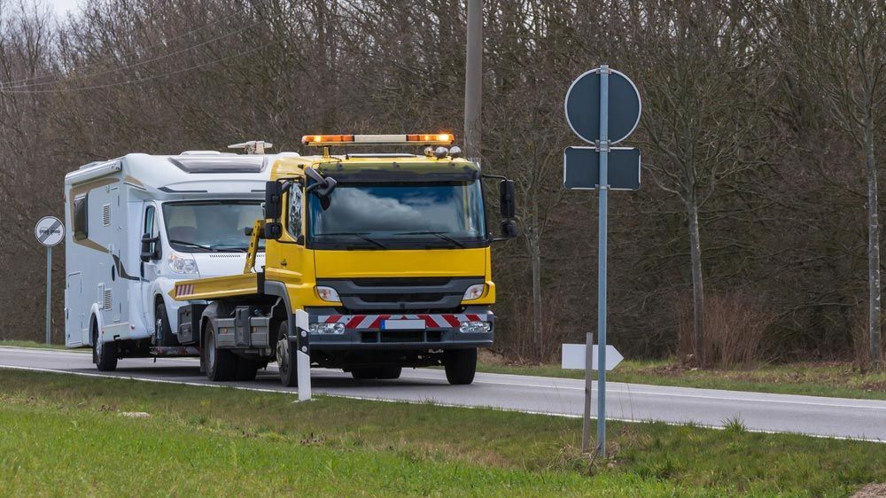 A Yellow Tow Truck Is Towing A Camper Down A Road — Tim's Towing and Transport In Sandgate, NSW