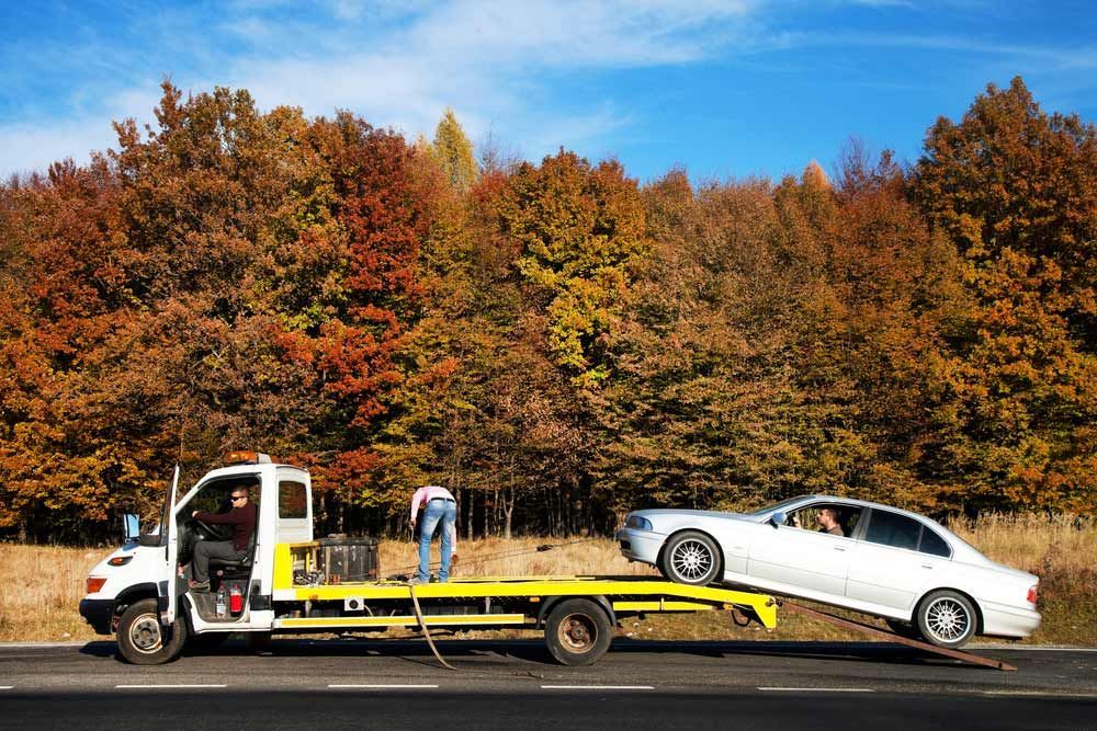 A Tow Truck Is Towing A White Car On The Side Of The Road — Tim's Towing and Transport In Mayfield, NSW