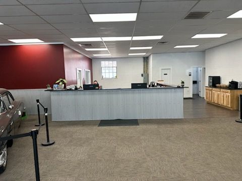 A gray commercial building with a black SUV parked in front, featuring a circular logo and several rectangular windows.