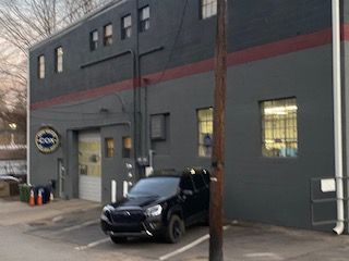 A gray commercial building with a black SUV parked in front, featuring a circular logo and several rectangular windows.