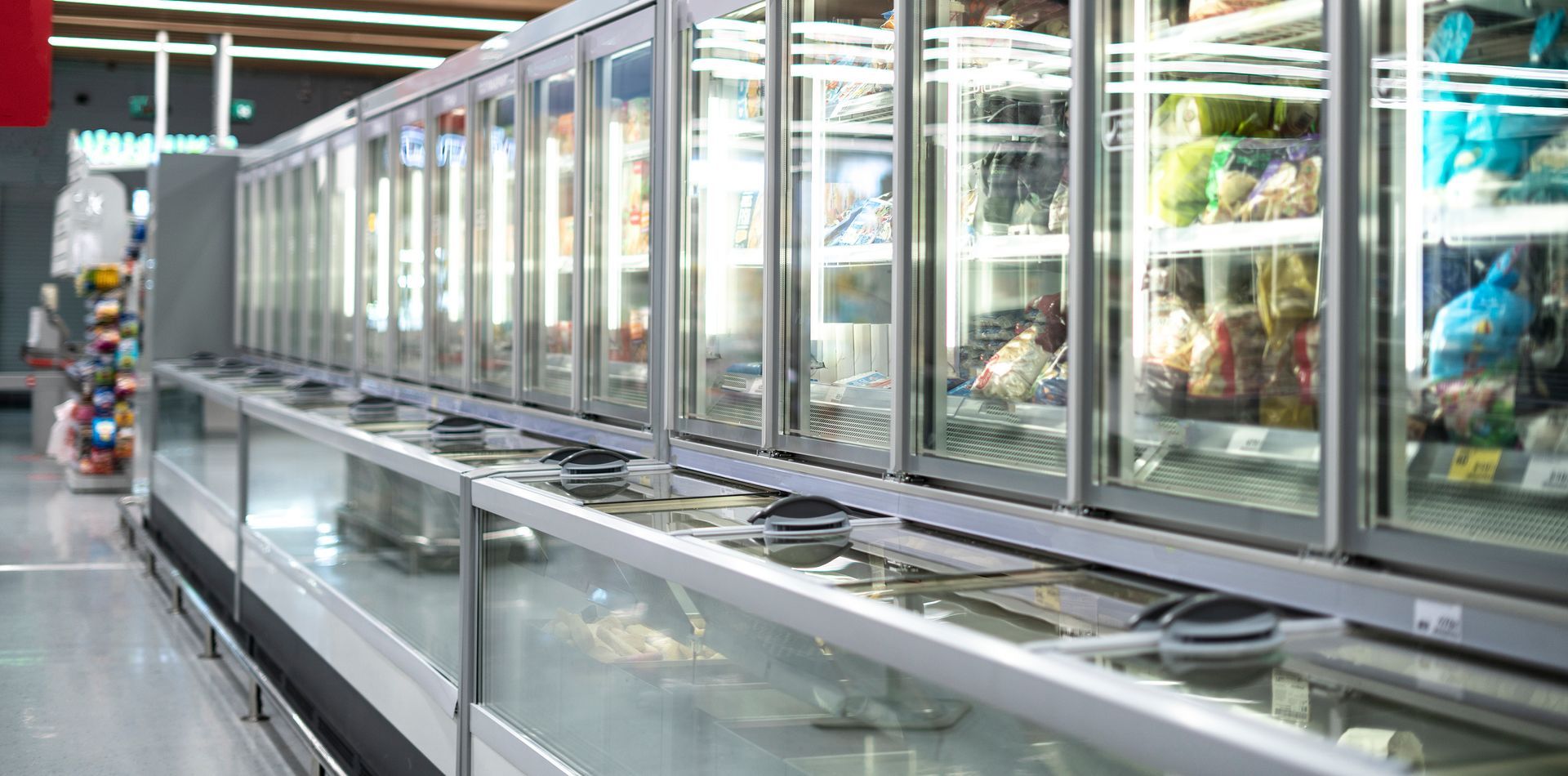 A row of refrigerators in a grocery store filled with food.