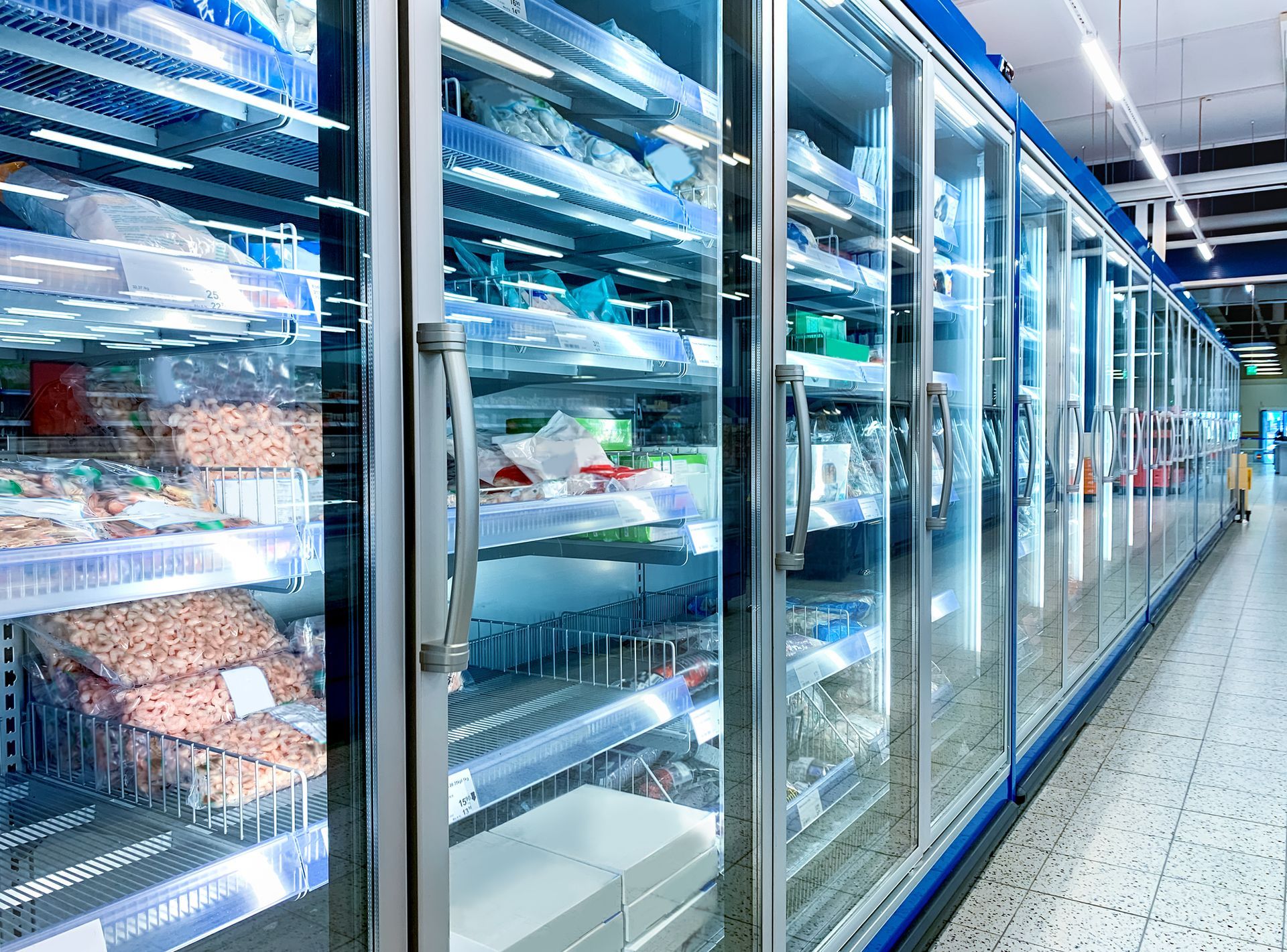 A row of commercial refrigerators in a supermarket filled with food.