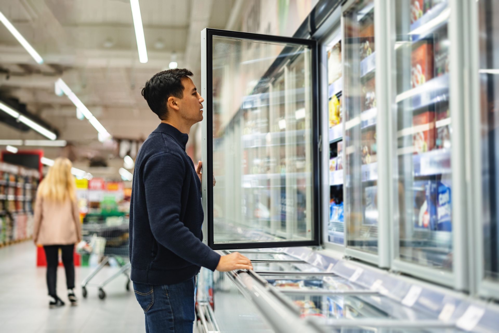 Man standing in front of commercial refrigerator in grocery store.