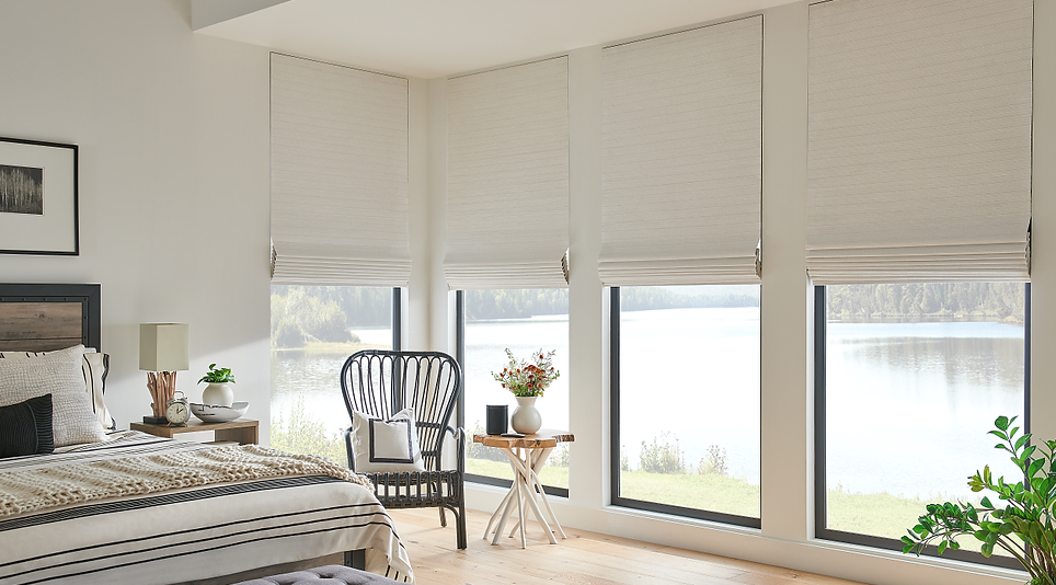 Bedroom with large windows, white blinds, a bed, chair, and table overlooking a lake.