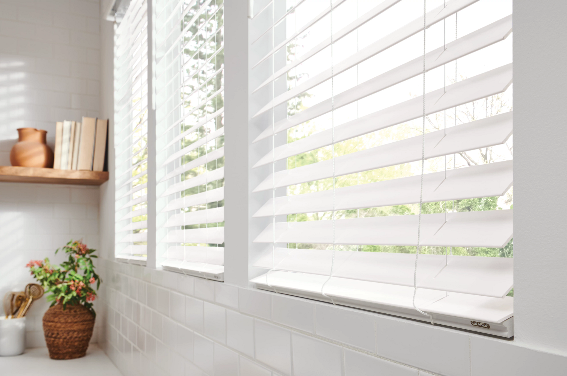 Kitchen sink under a window with wooden blinds and frame. Granite countertop and tiled backsplash.