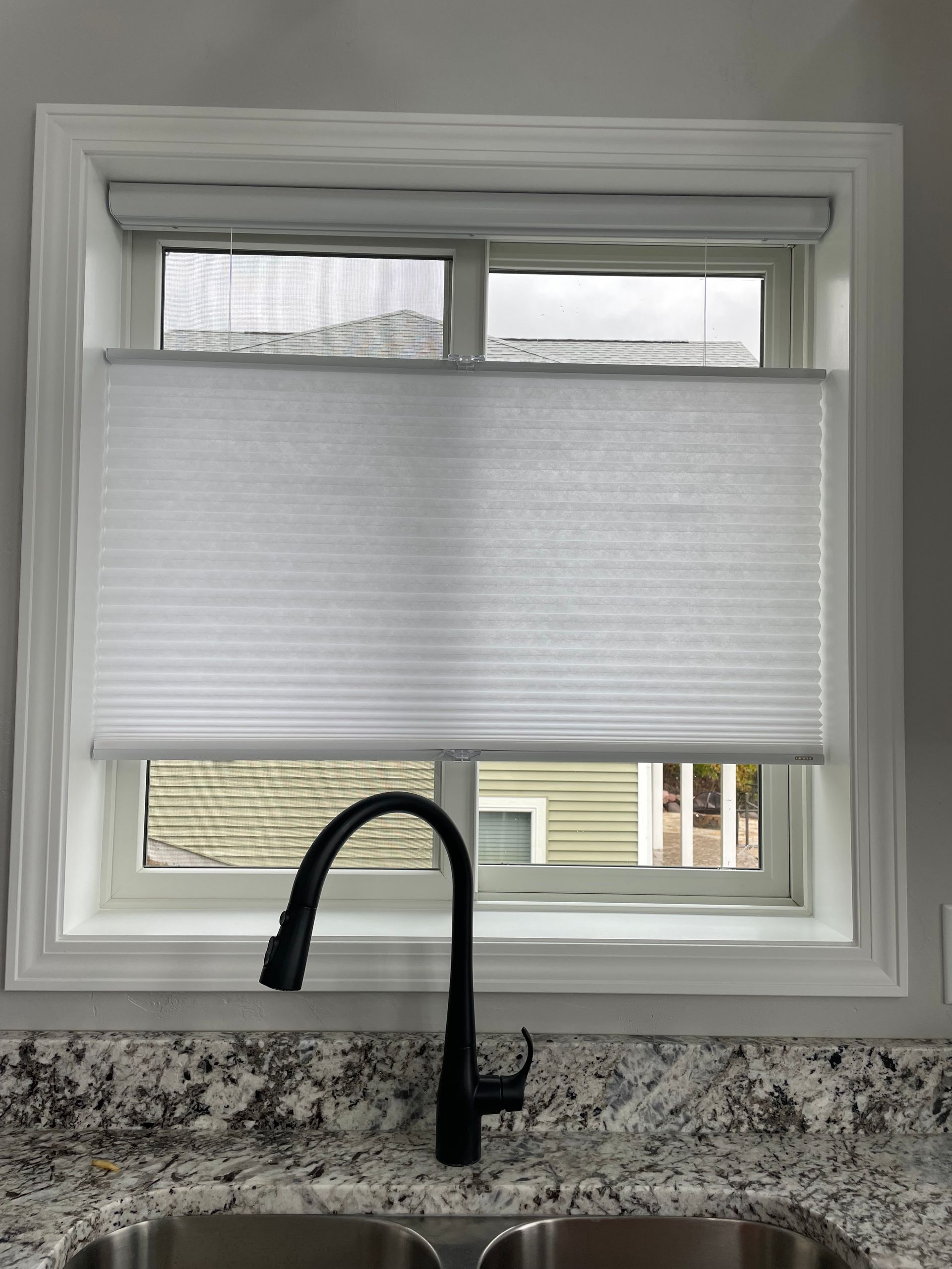 Kitchen window with white blinds, above a black faucet and granite countertop.