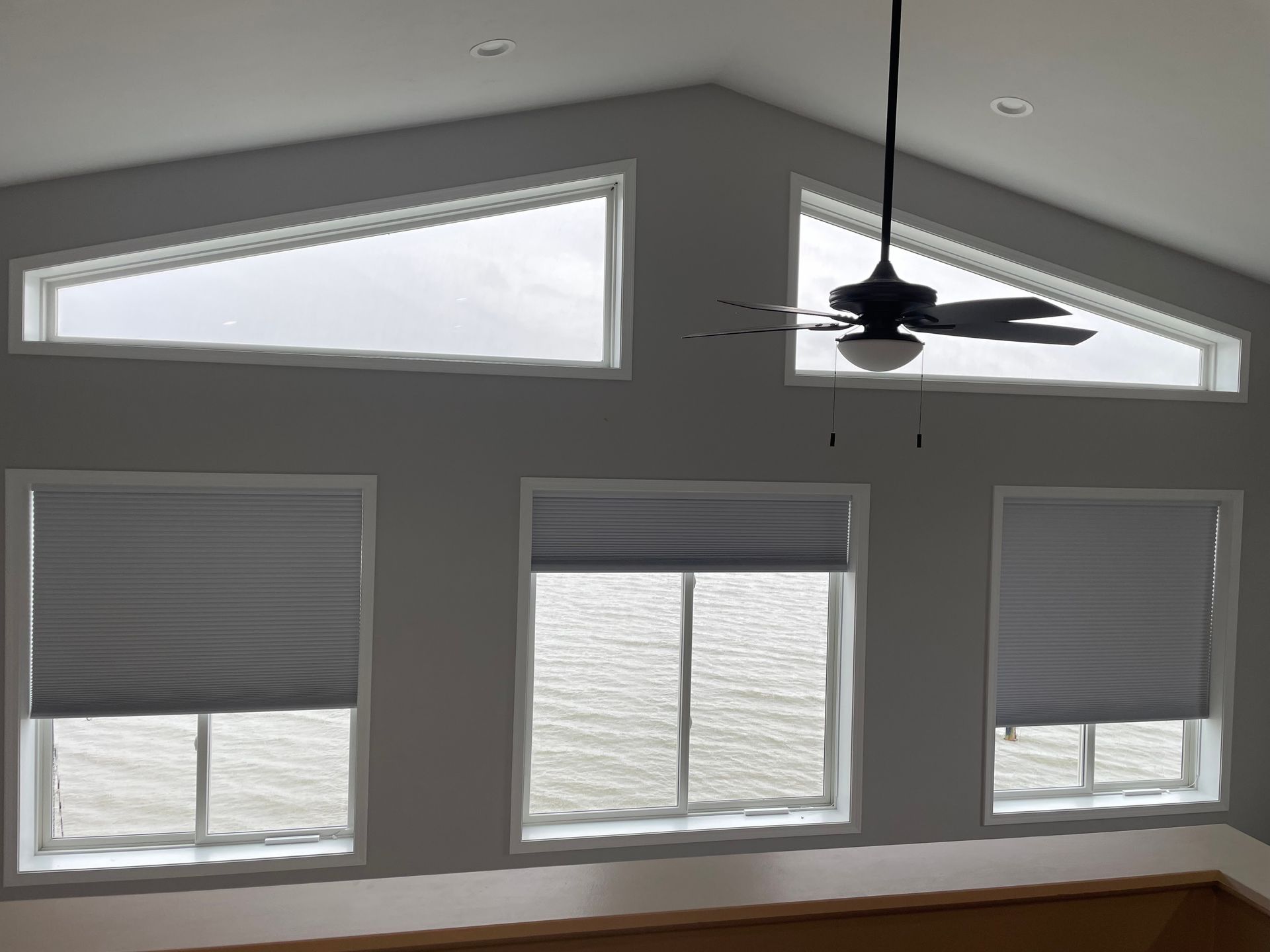Windows with grey shades, water view, and a ceiling fan.