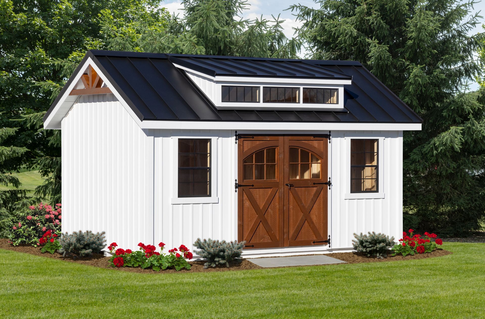 A white shed with a black roof is sitting in the middle of a lush green field.