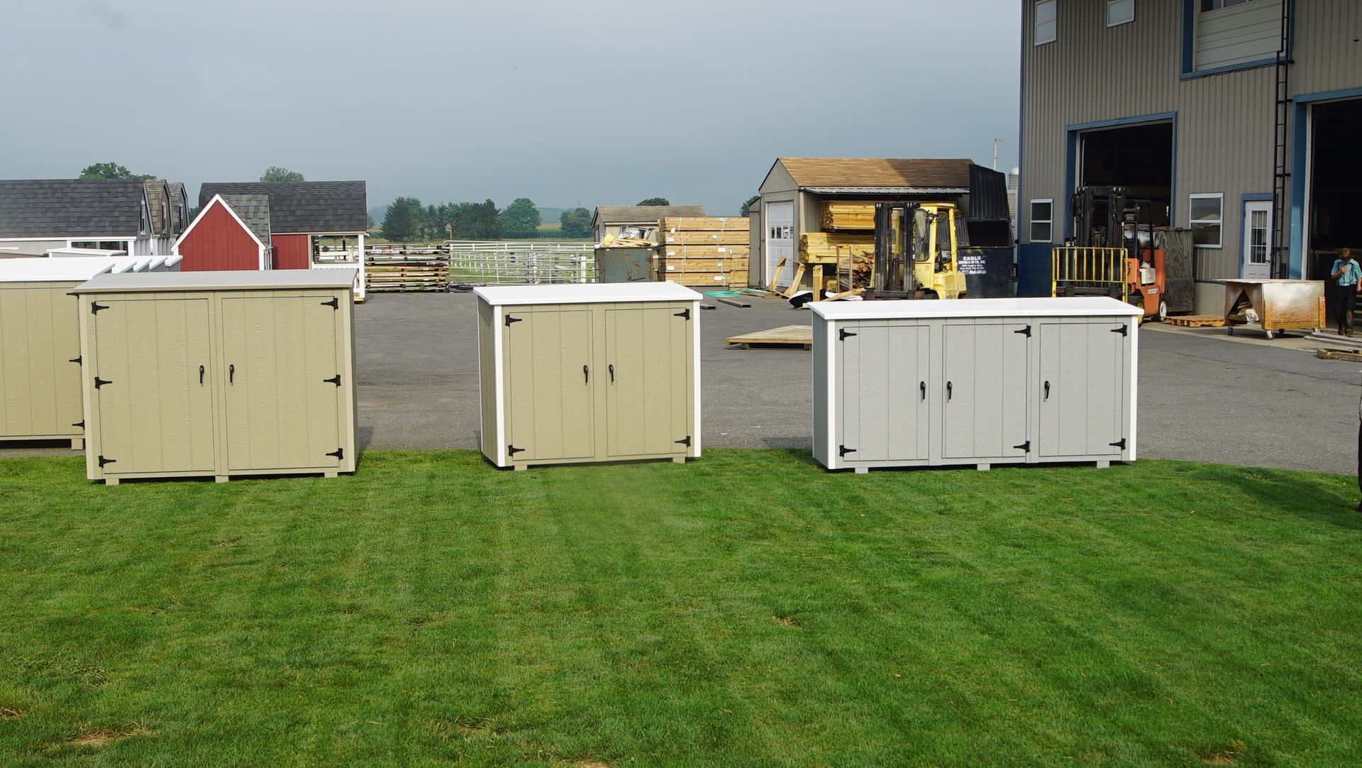 A row of sheds are lined up in a grassy area in front of a building