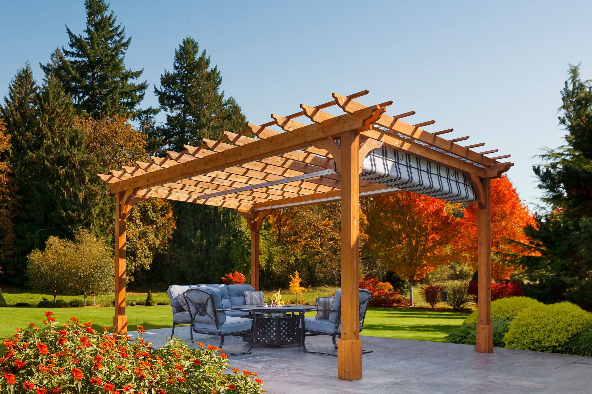 A wooden pergola over a patio seating area with a fire pit, set in a backyard garden during autumn.