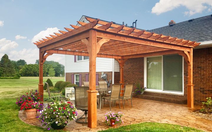 A wooden pergola is sitting on the side of a brick house.