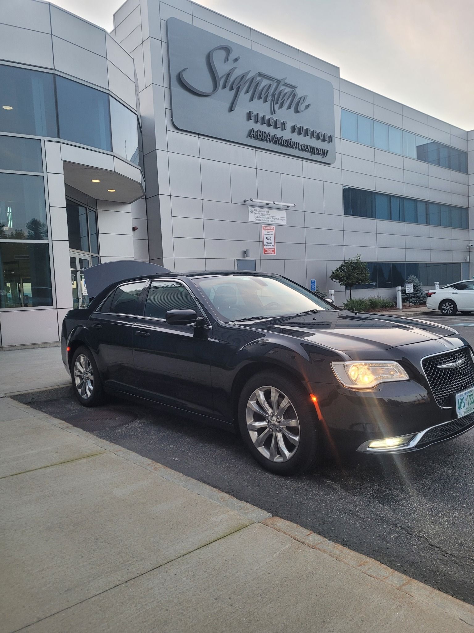 A black car is parked in front of a large building.