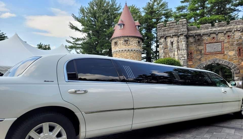 A white limousine is parked in front of a castle.