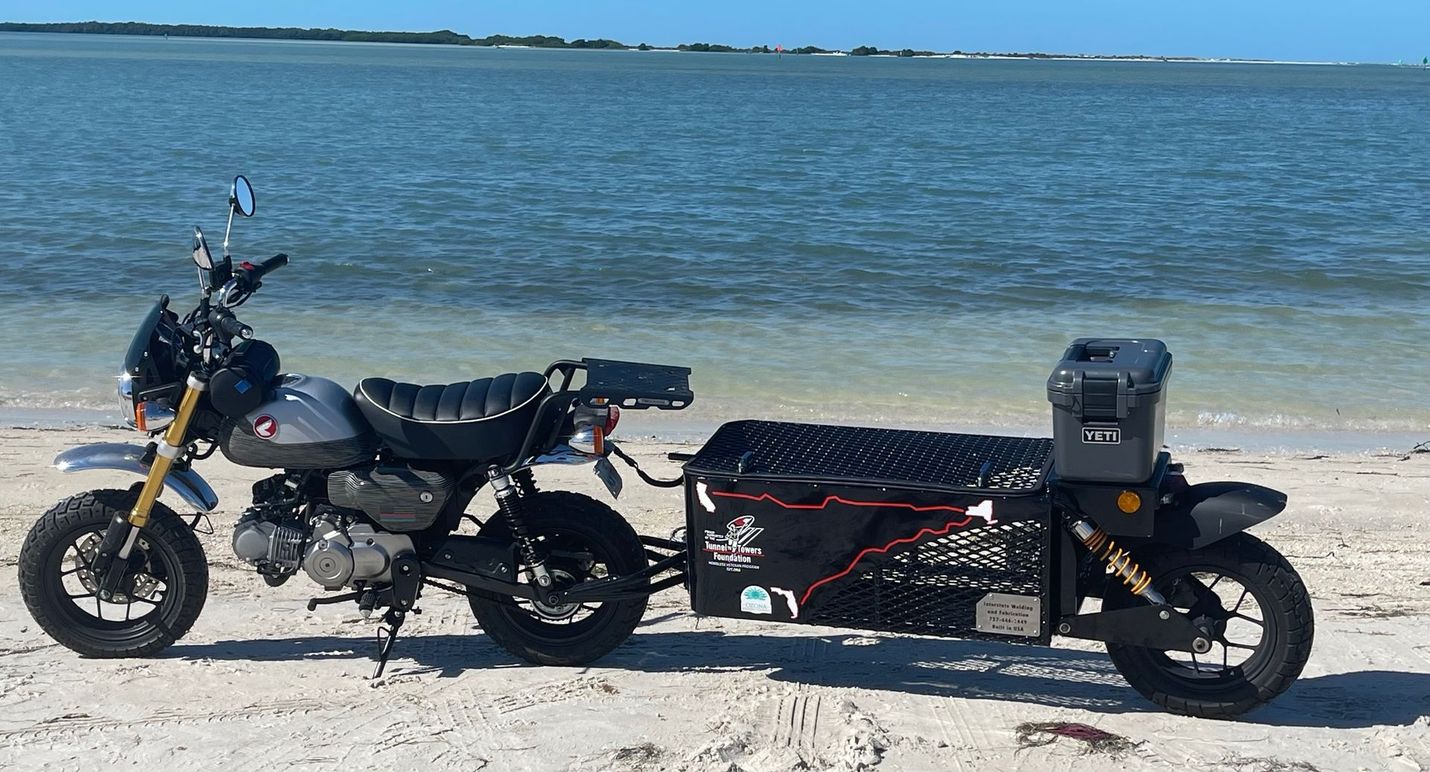 A motorcycle with a trailer attached to it is parked on the beach.