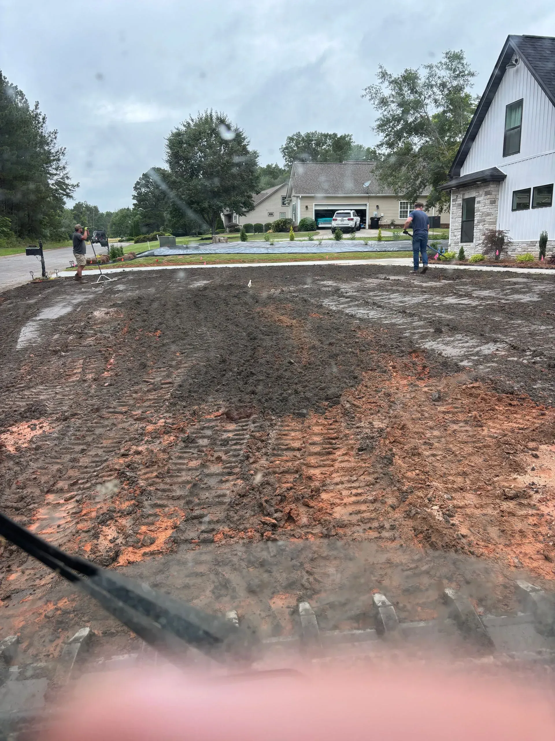 A front yard churned with dirt, likely for landscaping, with a person standing nearby. A house and sky in the background.