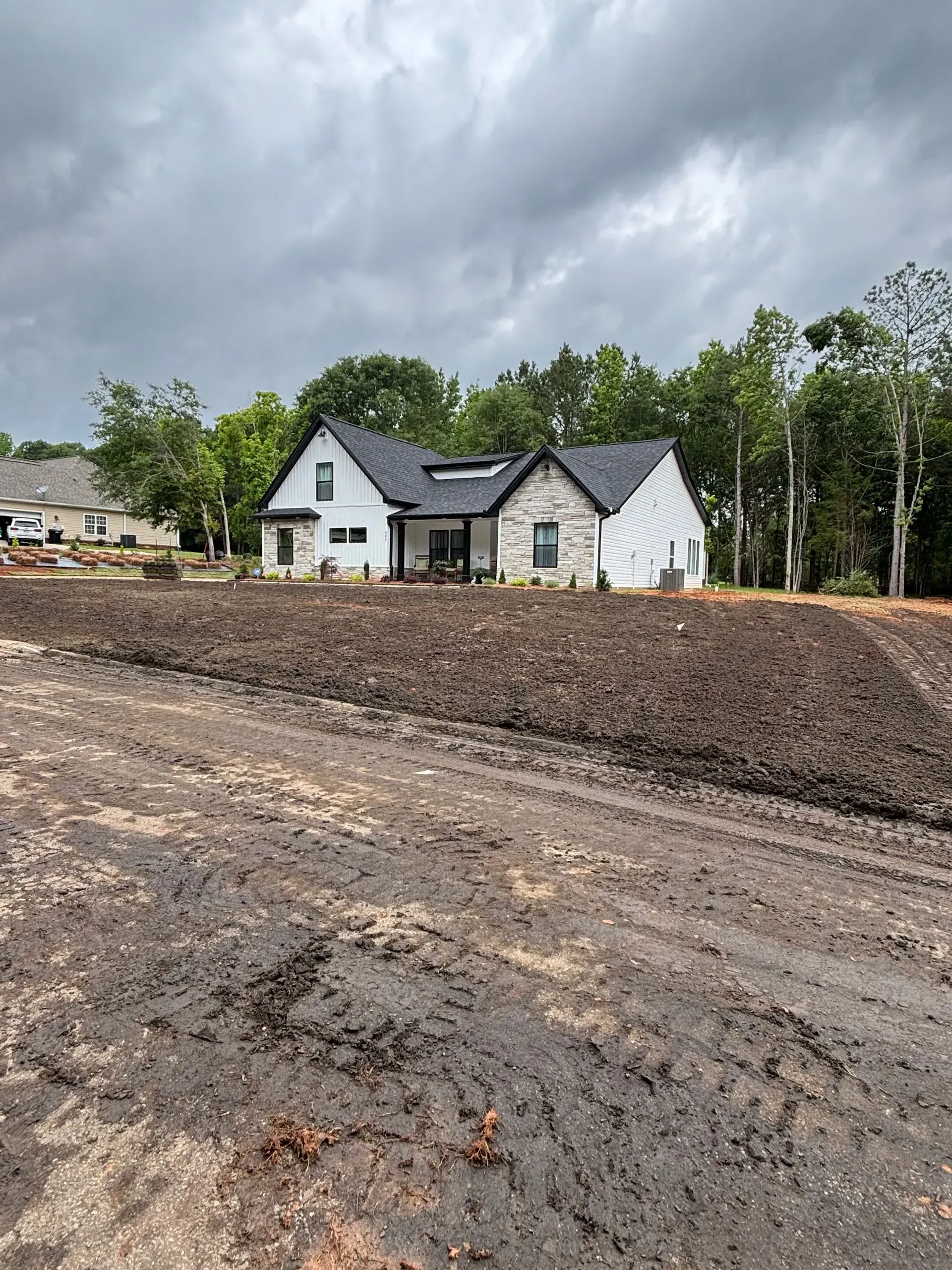 A new house with white siding and stone accents, set on a freshly graded lot under a cloudy sky.