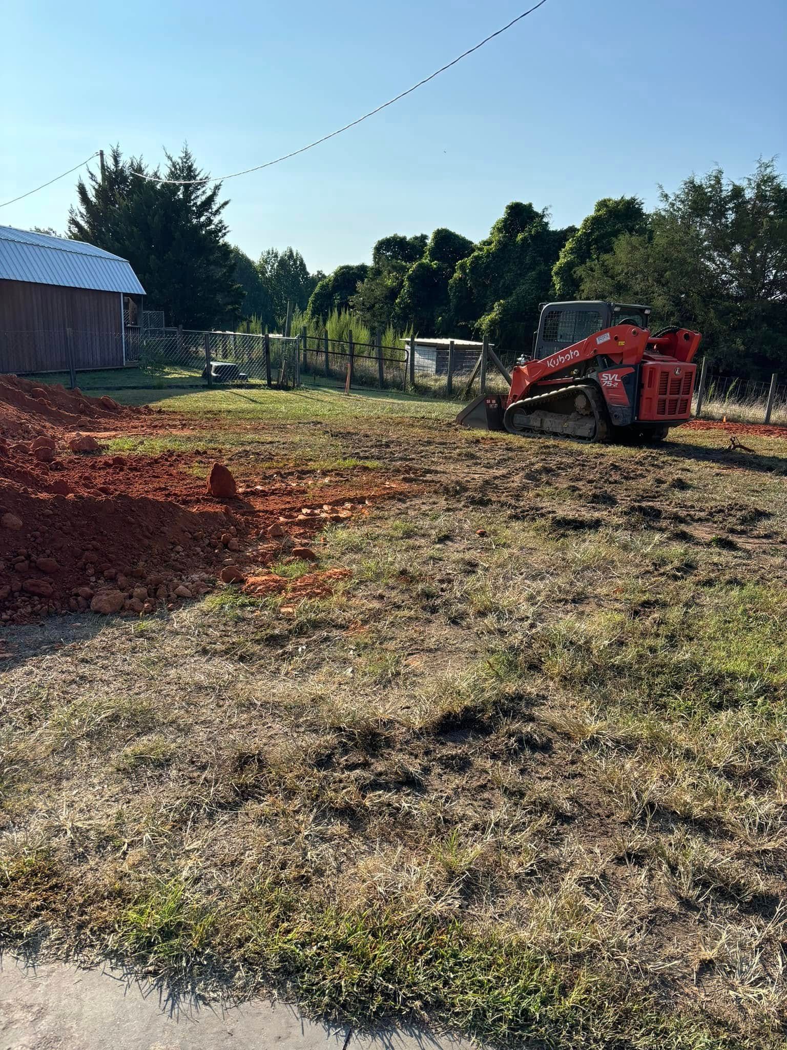 A red skid steer on a grassy area with a small mound of reddish dirt
