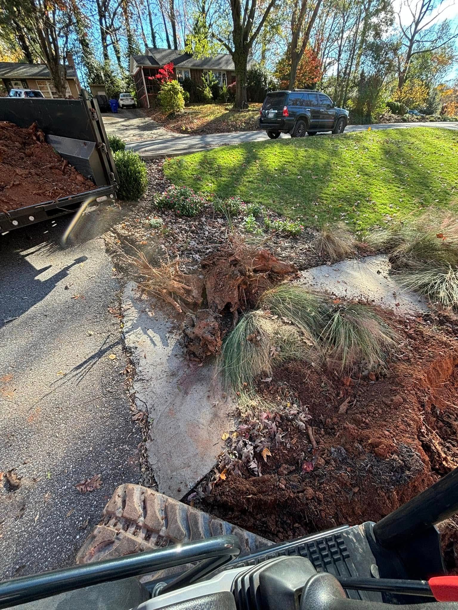 Bobcat unloading mulch onto a driveway, with green grass and houses in the background.