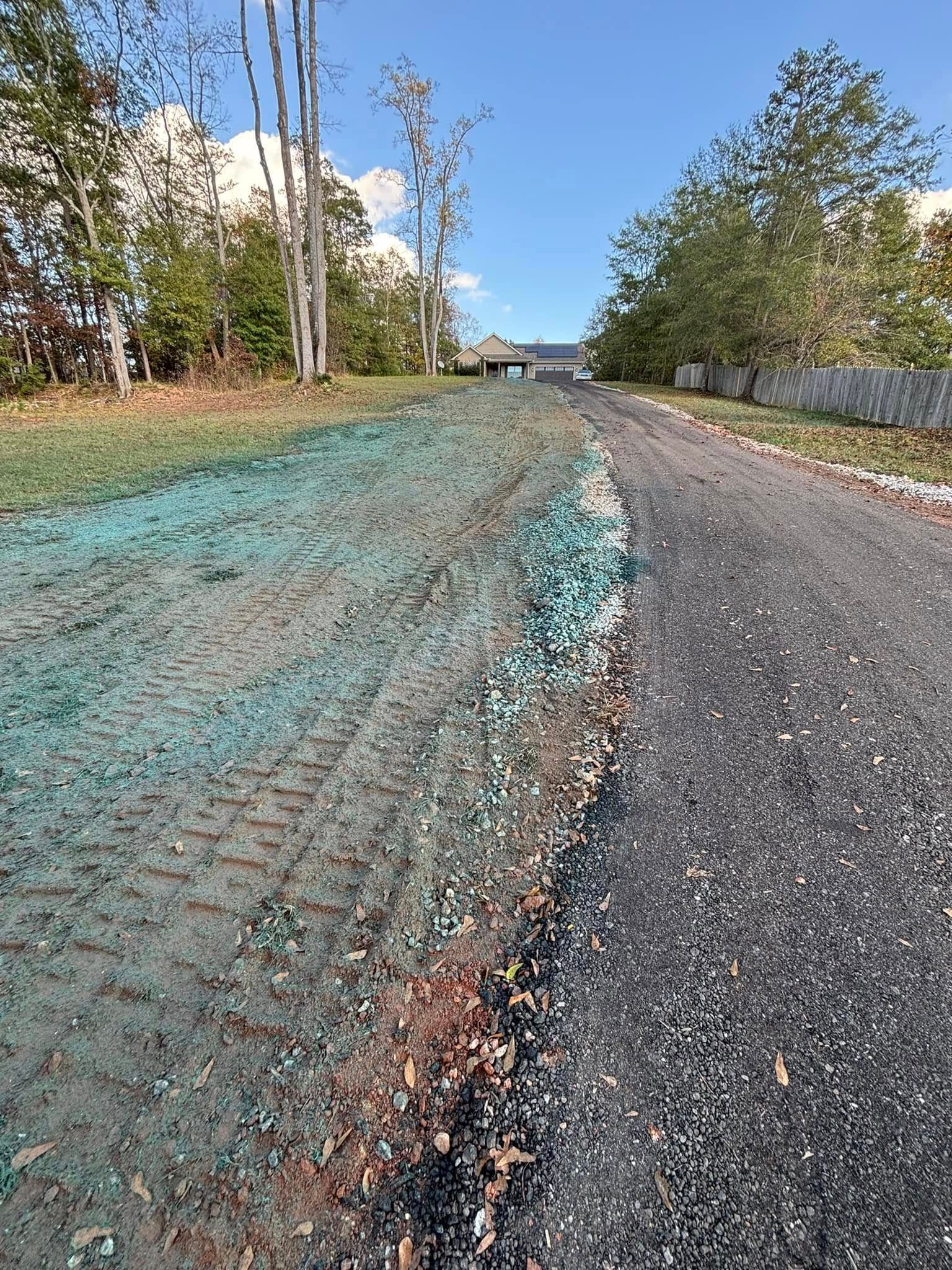 A gravel driveway leads uphill to a house, next to a grassy area treated with green seed protection.