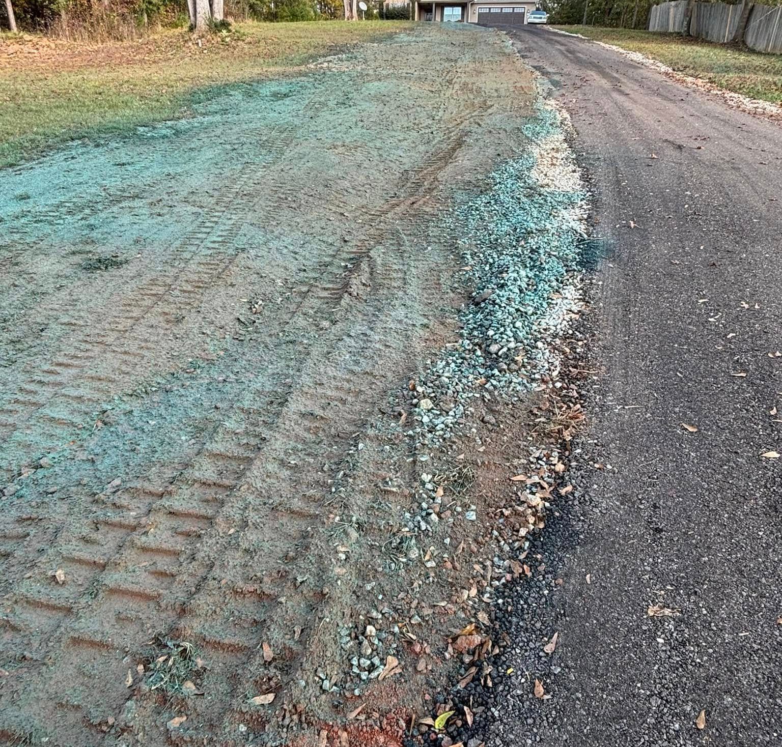 A driveway next to a grassy area recently seeded with a blue-green hydromulch, and a gray asphalt surface.