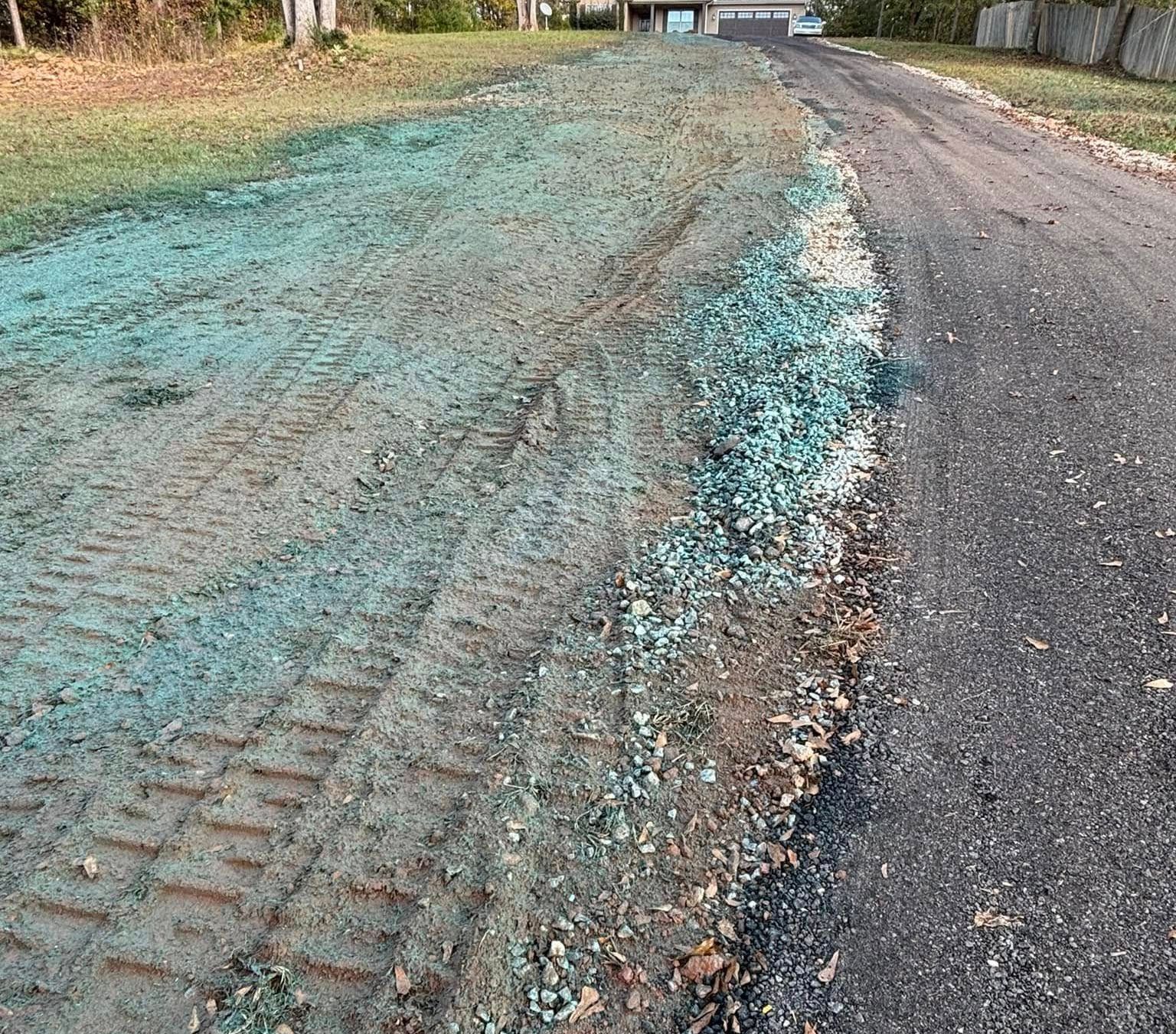 A gravel road with a section of freshly seeded, turquoise-colored earth on its side, marked by tire tracks.