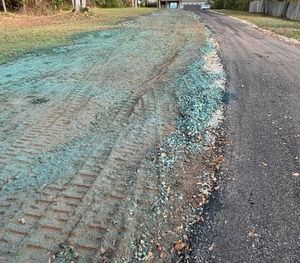 A gravel road with a section of freshly seeded, turquoise-colored earth on its side, marked by tire tracks.