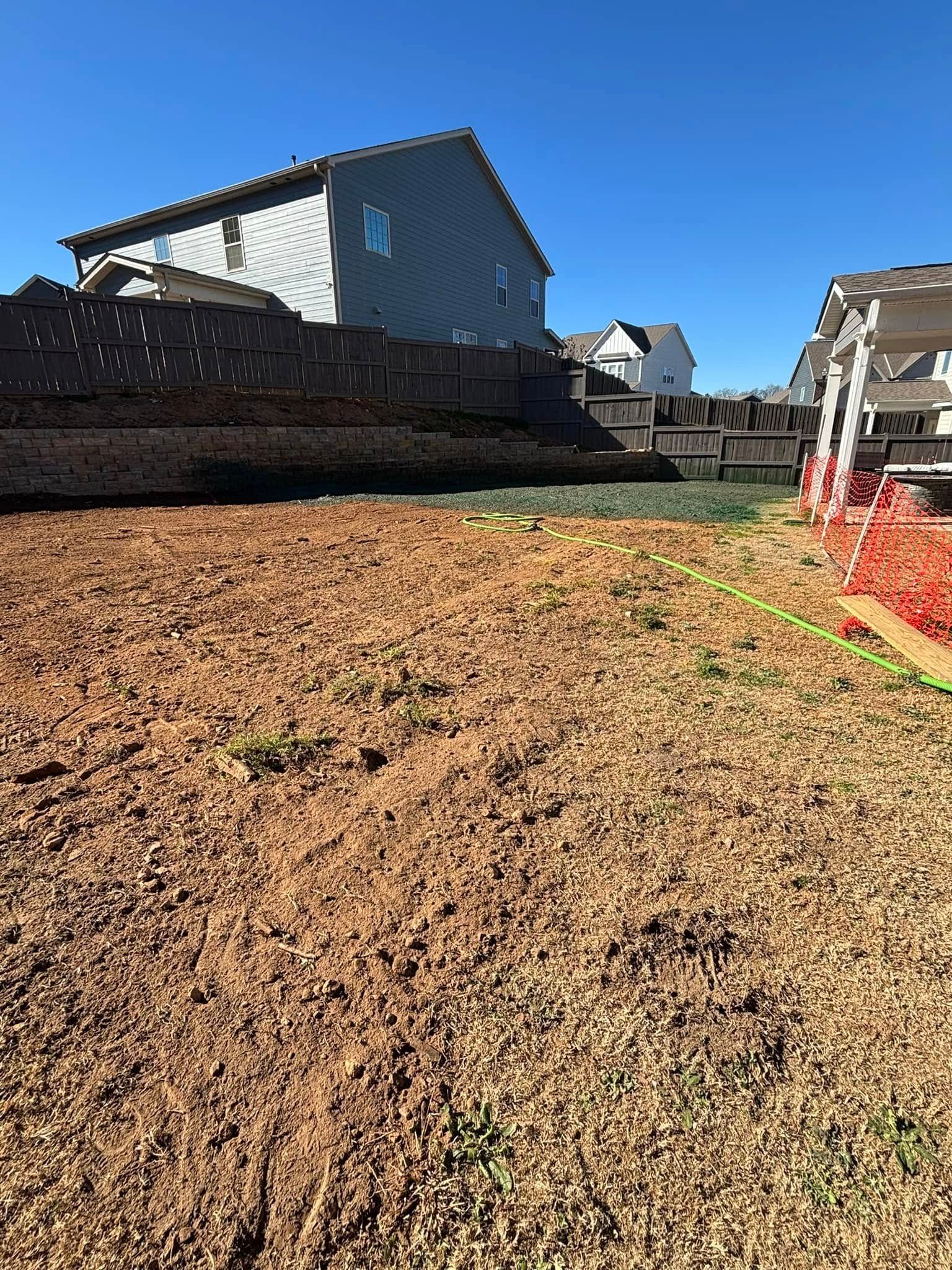 A backyard with bare soil, a retaining wall with a house behind it