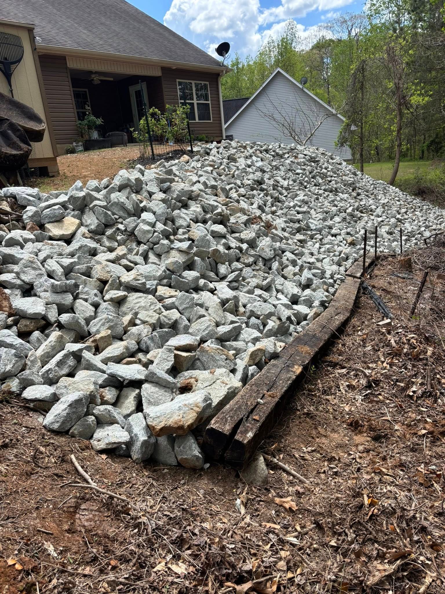 A large pile of gray rocks next to a weathered wooden border, likely for landscaping a backyard.