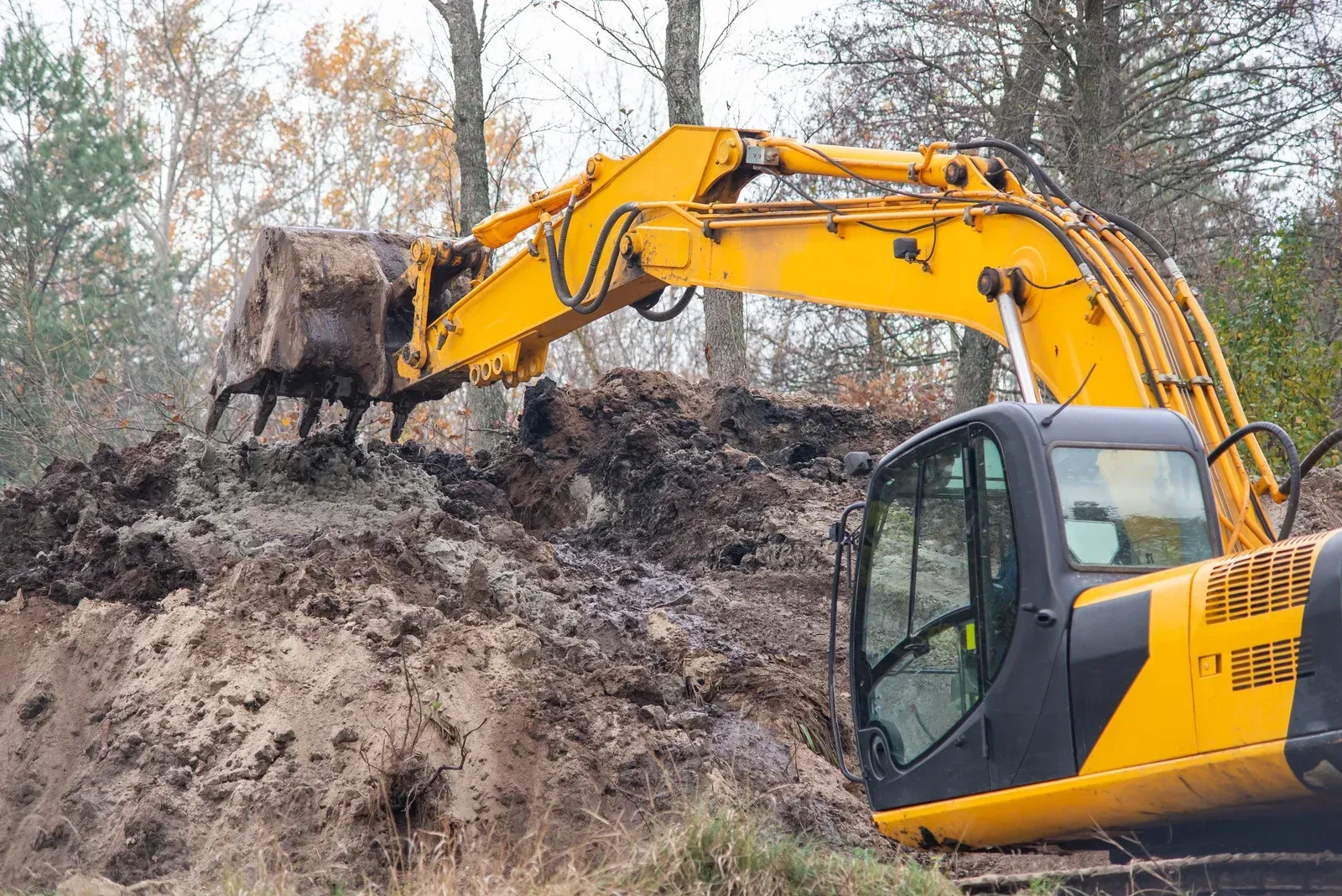 Yellow excavator digging into a pile of dirt; trees in background.