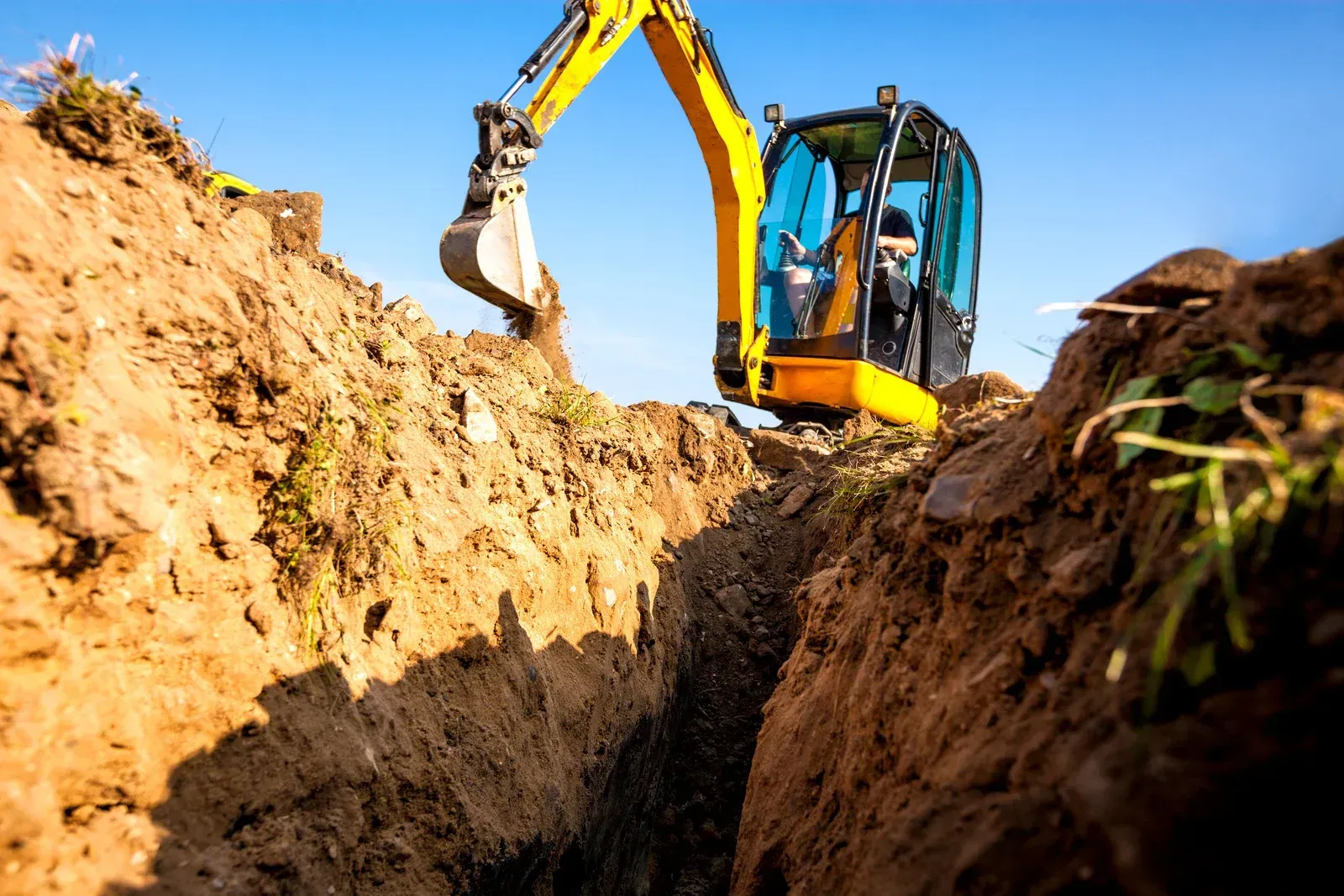 Demolition site with an excavator removing debris, sunny day, blue sky.