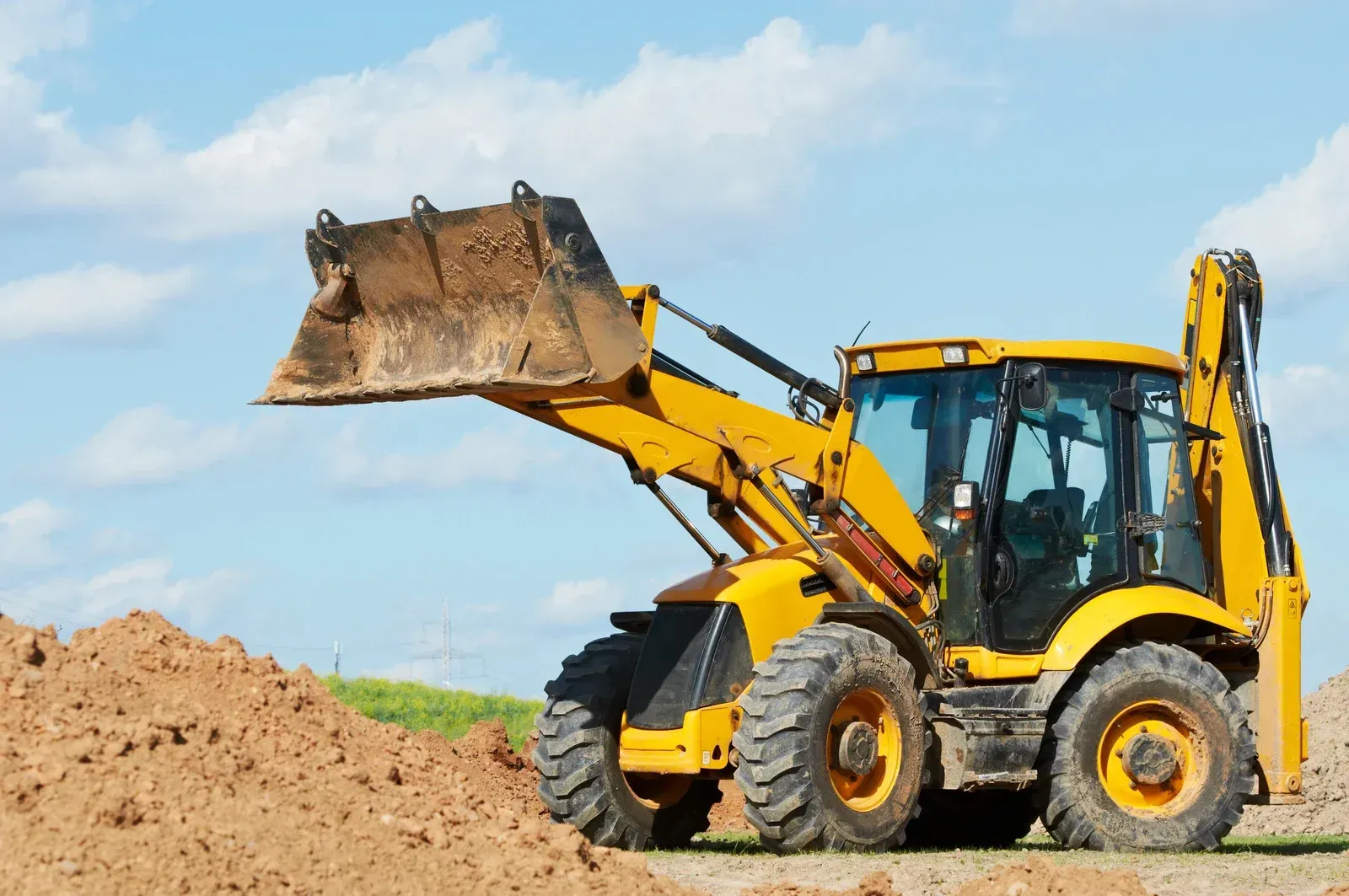 Yellow backhoe loader with bucket raised, working on a construction site.
