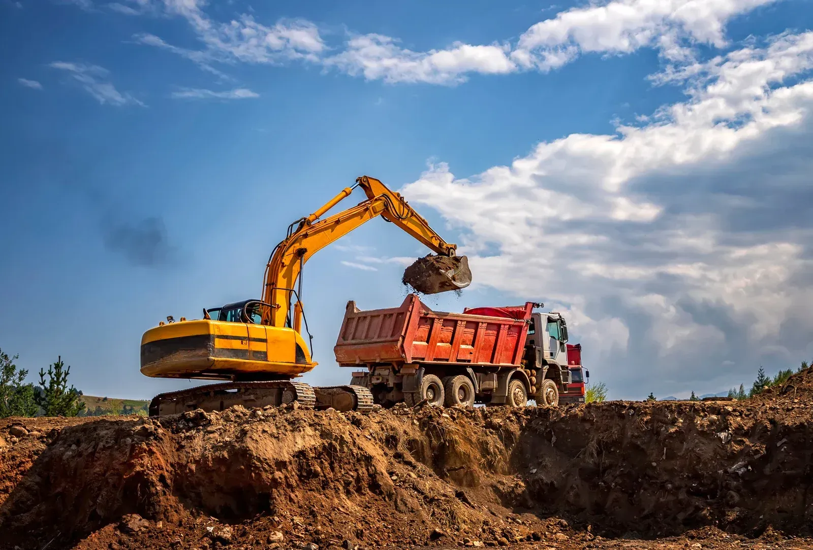 A red excavator demolishes a building on a sunny day, surrounded by debris and fallen leaves.