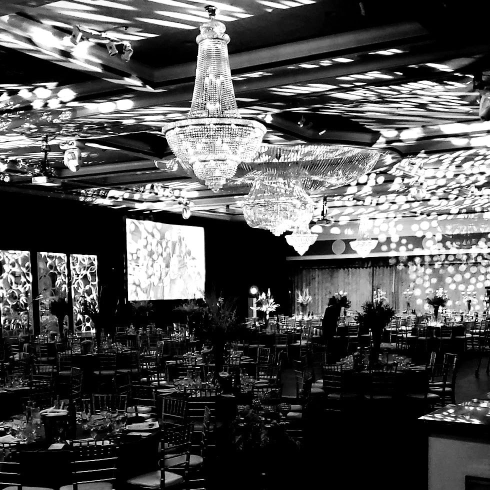 a black and white photo of a large room with tables and chairs and a chandelier hanging from the ceiling .