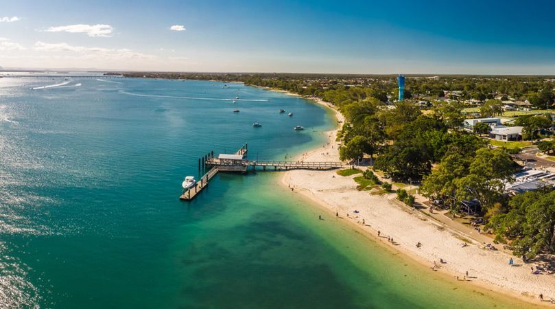 An Aerial View of a Beach With a Pier and a Lighthouse — A Grade Tree Services in Bribie Island, QLD