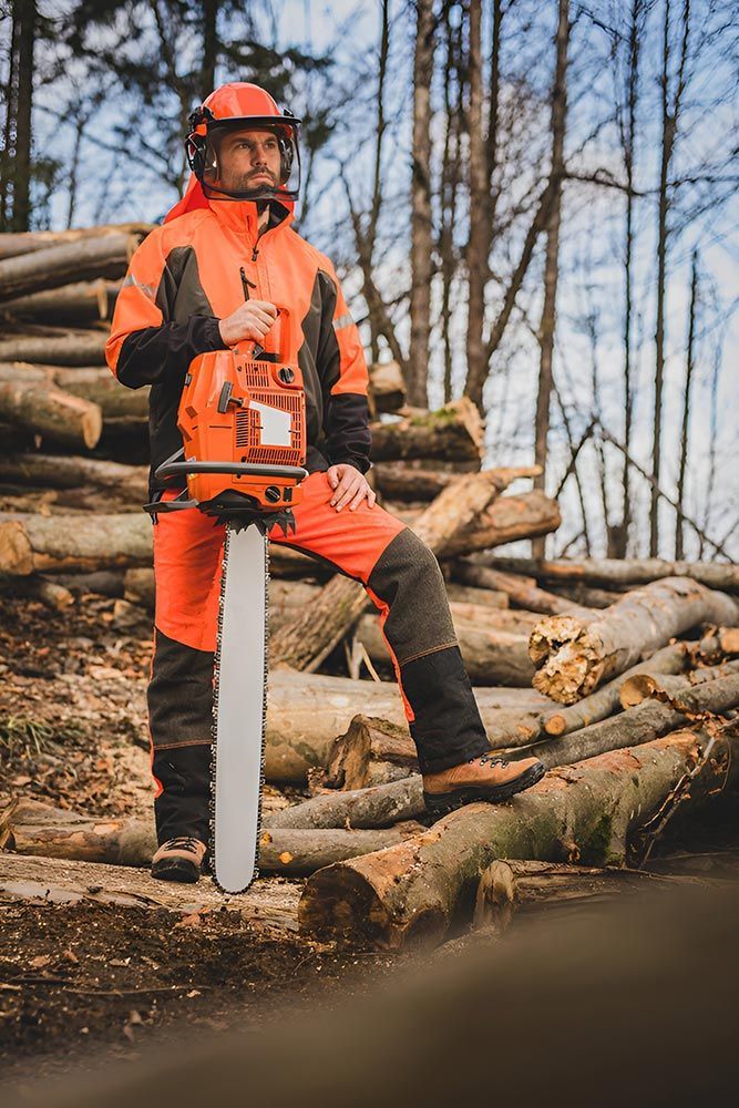 A Man is Standing Next to a Pile of Logs Holding a Chainsaw — A Grade Tree Services in Caboolture, QLD