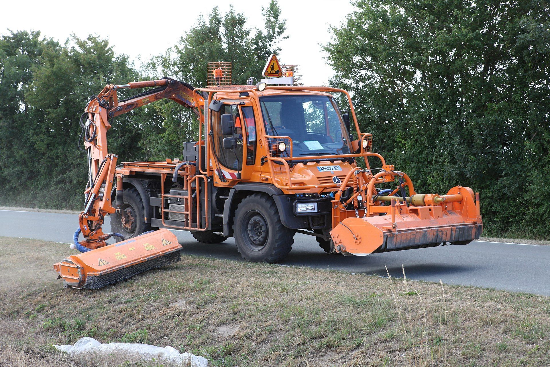 Photograph of a Mercedes Unimog utility vehicle, fitted with front and boom mounted flail mowers.