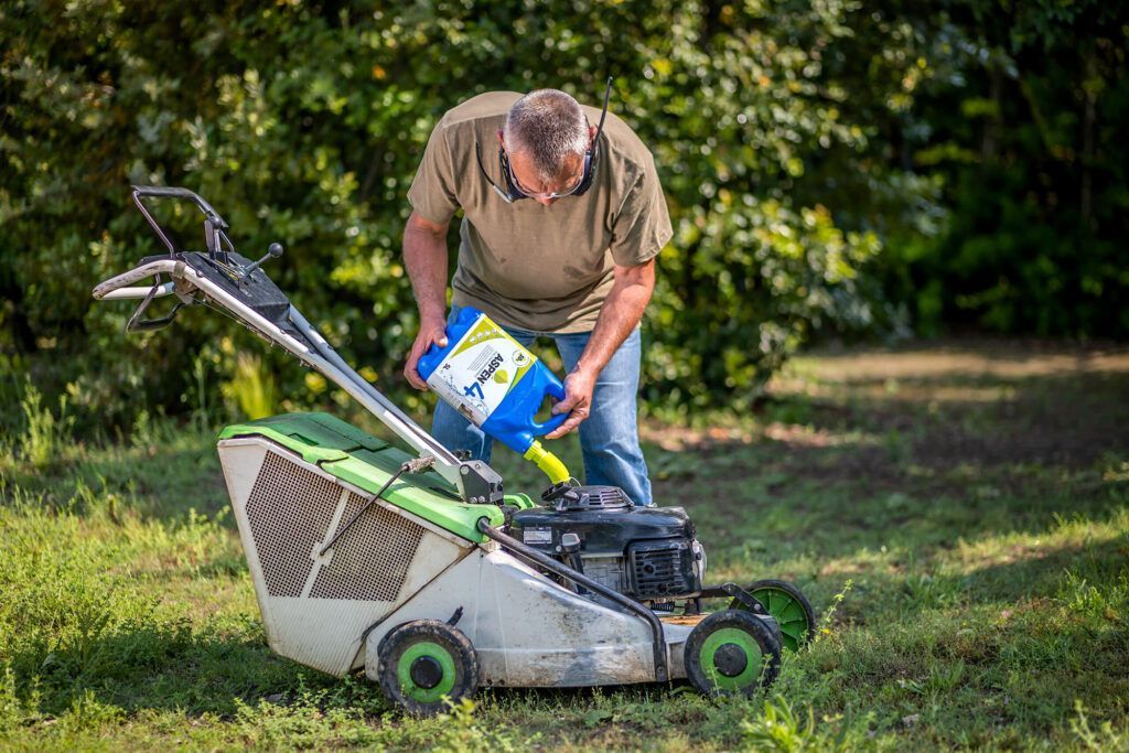 Photograph of a man pouring Aspen4 alkalyte petrol into the petrol storage tank of a lawnmower.