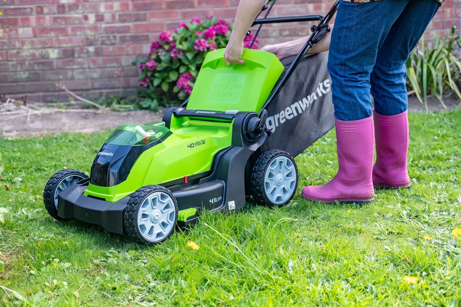 Photograph of a woman removing the grass collector from a Geenworks brand, cordless, electric, lawn mower.