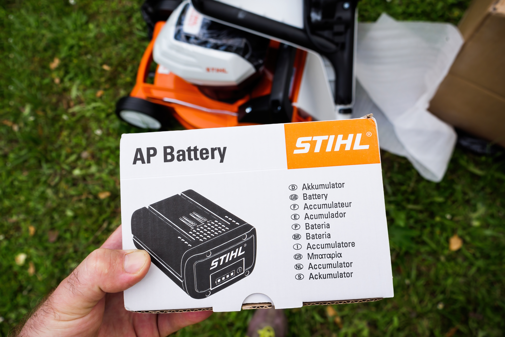 Photograph of an instruction manual for a Stihl AP series battery, with a Stihl cordless li-ion lawnmower in the background.