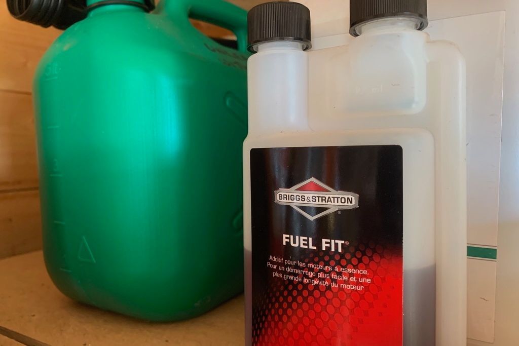 Photograph of a bottle of Briggs & Stratton Fuel Fit petrol stabiliser, beside a green plastic petrol storage container.