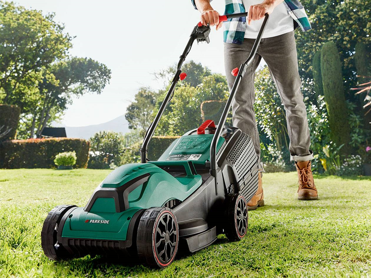 Photograph of a man cutting grass using a Lidl Parkside branded corded electric lawnmower.