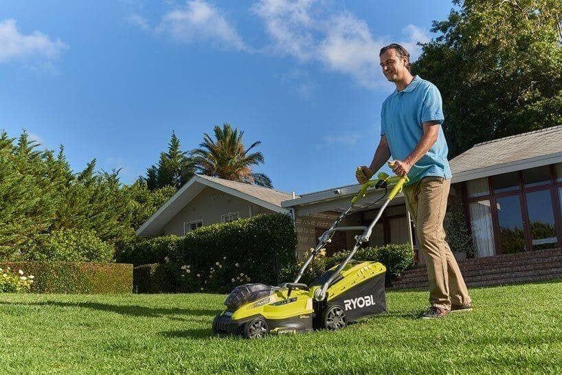 Man cutting a lawn with a Ryobi Fusion hybrid lawnmower.