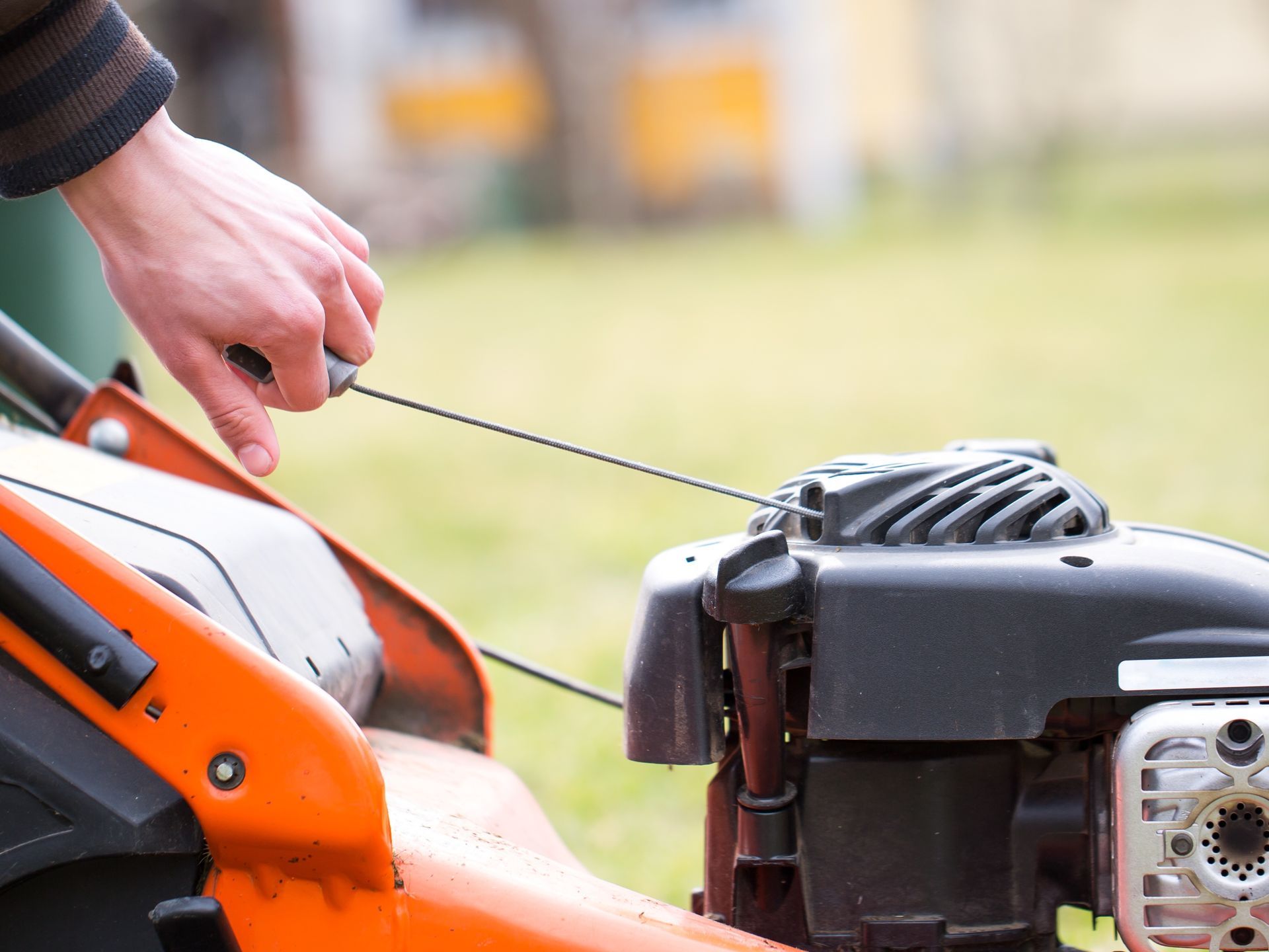 Photograph of a man starting a petrol lawnmower, using a recoil start mechanism.