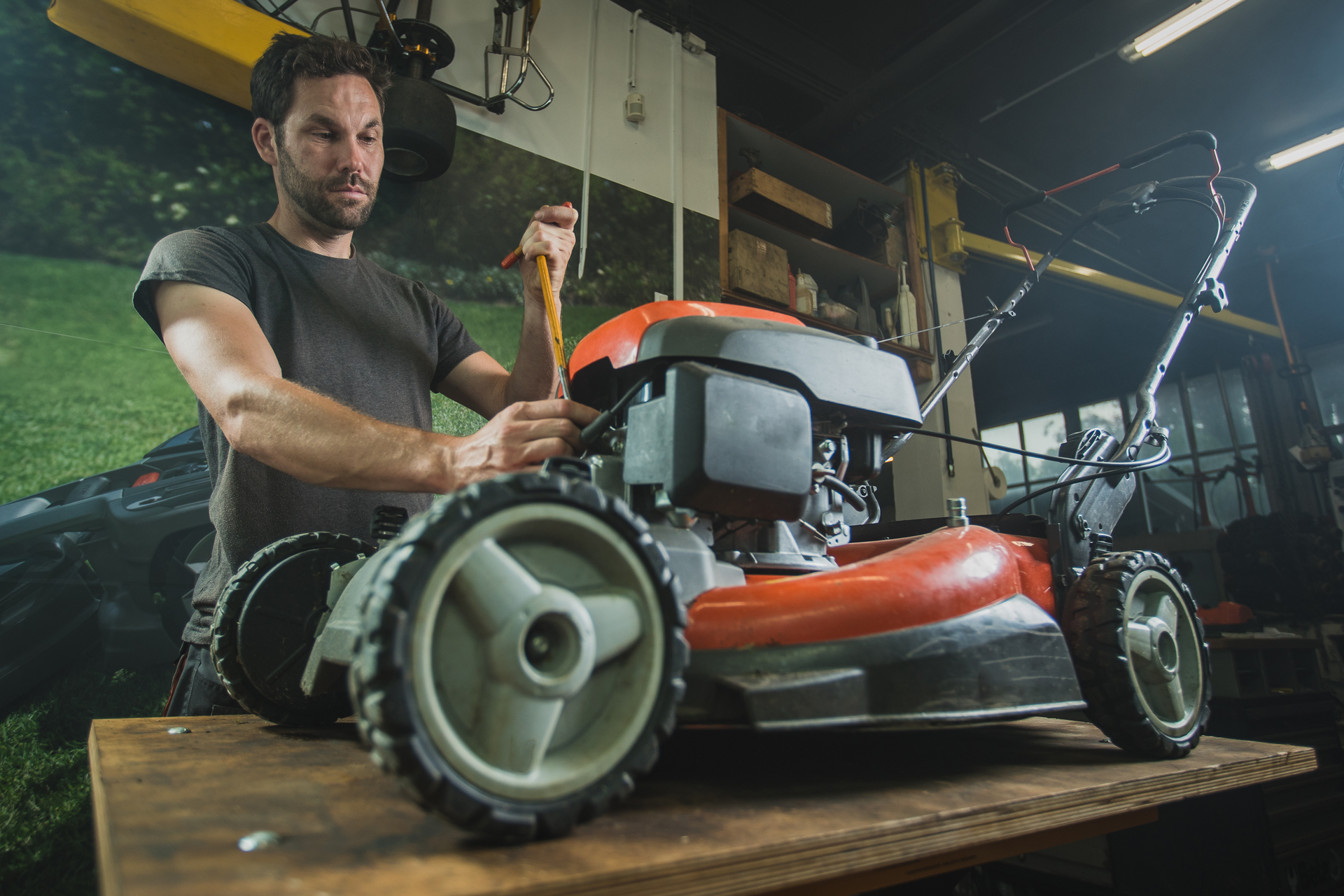 Photograph of a man servicing a lawnmower, positioned on a workbench.